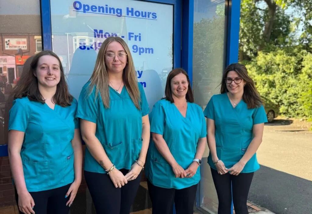 Four central pharmacy team members smiling whilst standing in front of Central Pharmacy's entrance on a sunny day.