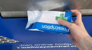 A person's hand reaching into the hatch to retrieve a prescription from the 24/7 collection point.