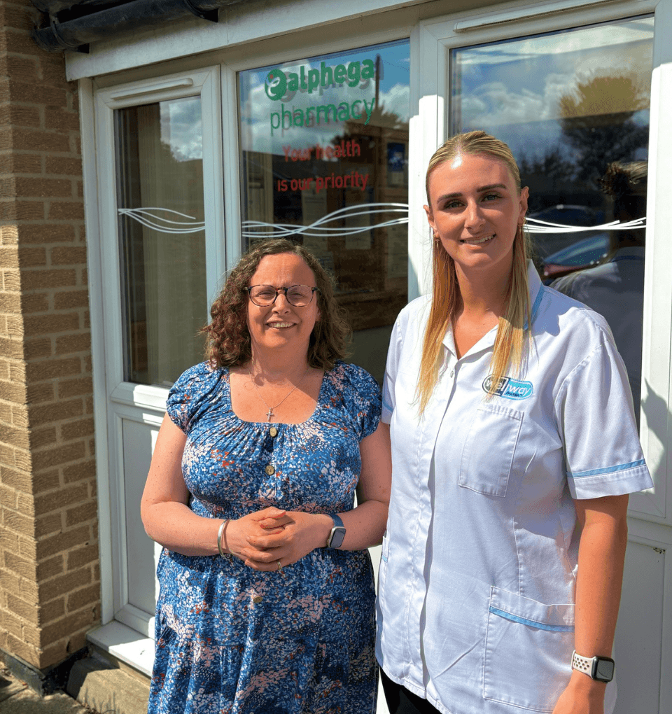Pegswood Pharmacy Management Our Pharmacist Sharon and Technician Jess beaming outside of Pegswood Pharmacy on a sunny day.